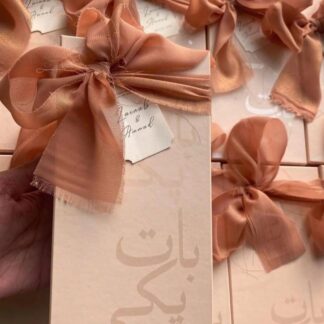 Blush pink Baat Pakki favor boxes with oversized fabric bows and personalized tags for Pakistani engagement celebrations.