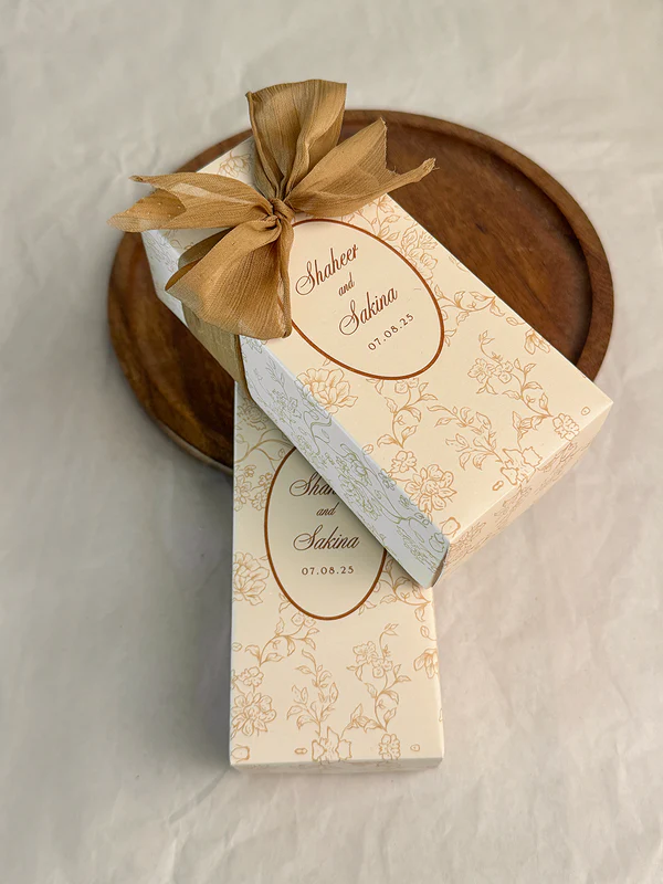 Ivory rectangular Nikkah favor box with delicate gold floral design, personalized couple details and satin ribbon for Pakistani weddings.