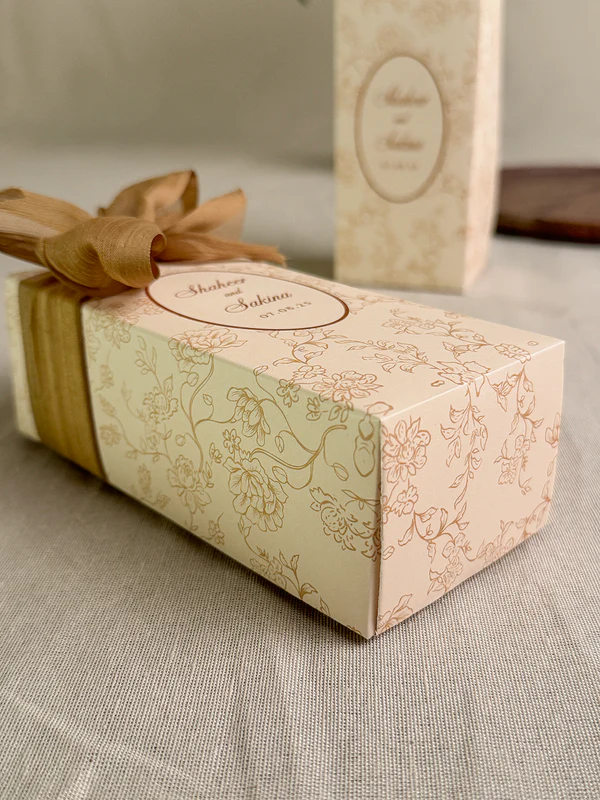 Ivory rectangular Nikkah favor box with delicate gold floral design, personalized couple details and satin ribbon for Pakistani weddings.