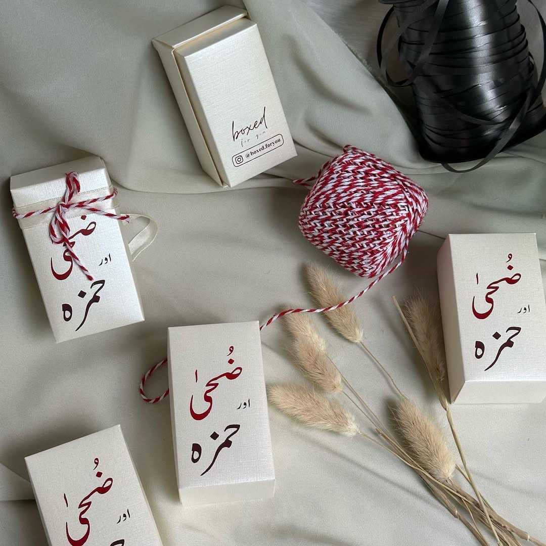 Personalized ivory mini sweet favor boxes with custom Arabic calligraphy and brown ribbon, filled with traditional sweets for a Nikkah or Muslim wedding celebration.