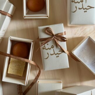Personalized ivory mini sweet favor boxes with custom Arabic calligraphy and brown ribbon, filled with traditional sweets for a Nikkah or Muslim wedding celebration.