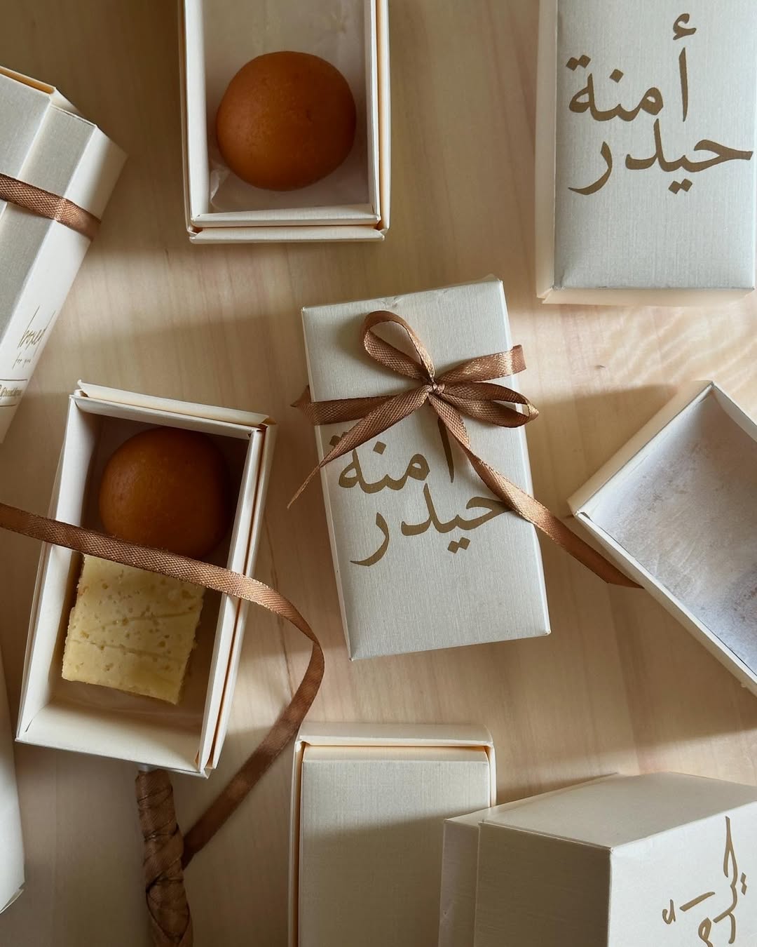 Personalized ivory mini sweet favor boxes with custom Arabic calligraphy and brown ribbon, filled with traditional sweets for a Nikkah or Muslim wedding celebration.