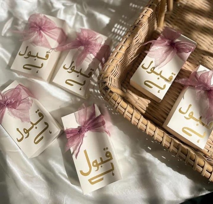 White Qabool Hai favor boxes with gold lettering and blush pink organza ribbon bows for Nikkah ceremonies, Muslim weddings and Pakistani wedding celebrations.
