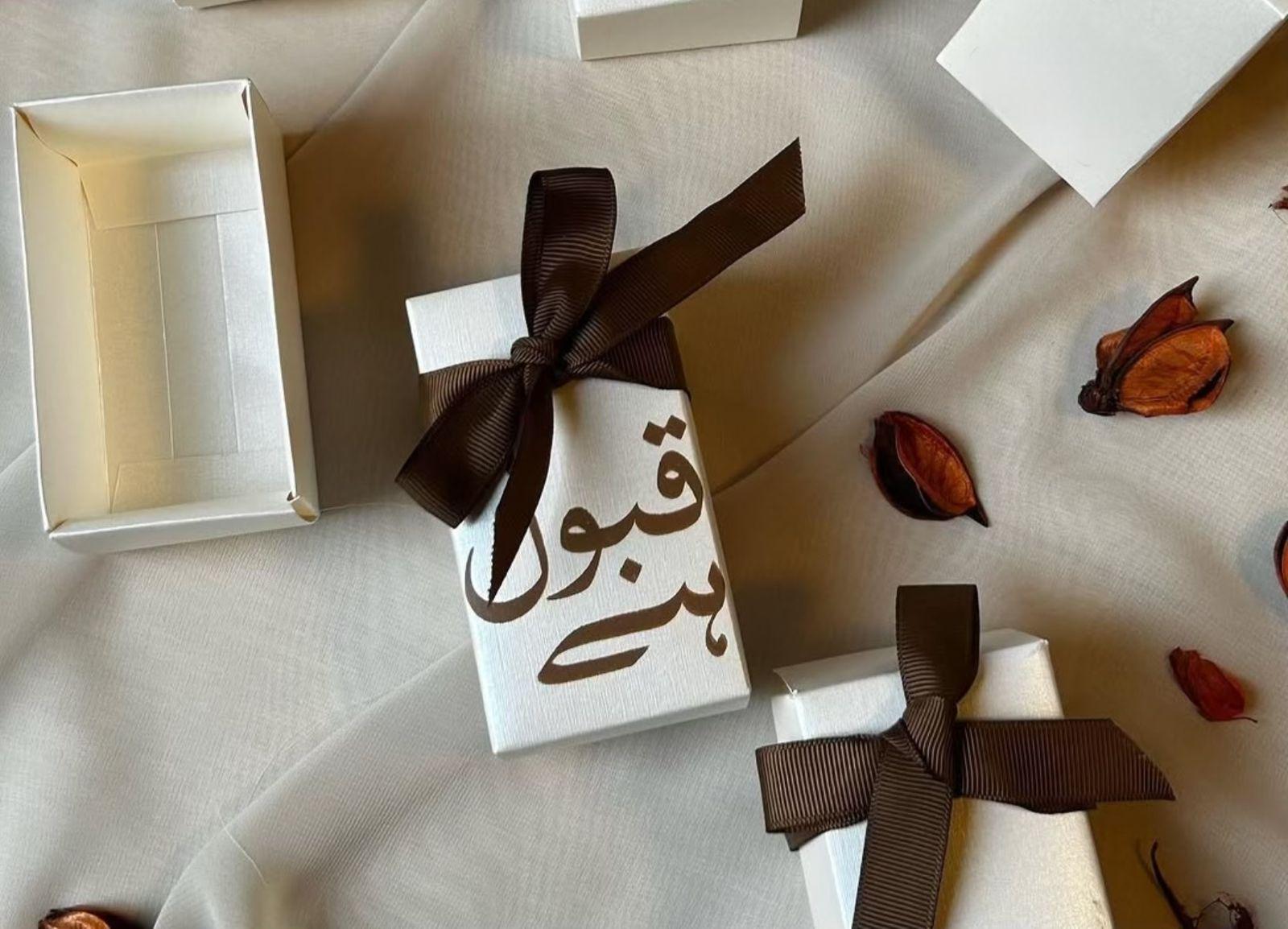 Ivory Qabool Hai favor boxes with Urdu calligraphy and brown ribbon for Pakistani Nikkah and Muslim wedding celebrations.
