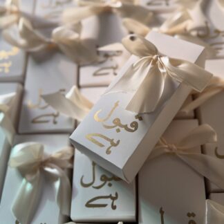 Ivory Qabool Hai mithai favor boxes with gold Urdu calligraphy and satin bows for Pakistani Nikkah and Muslim wedding celebrations.