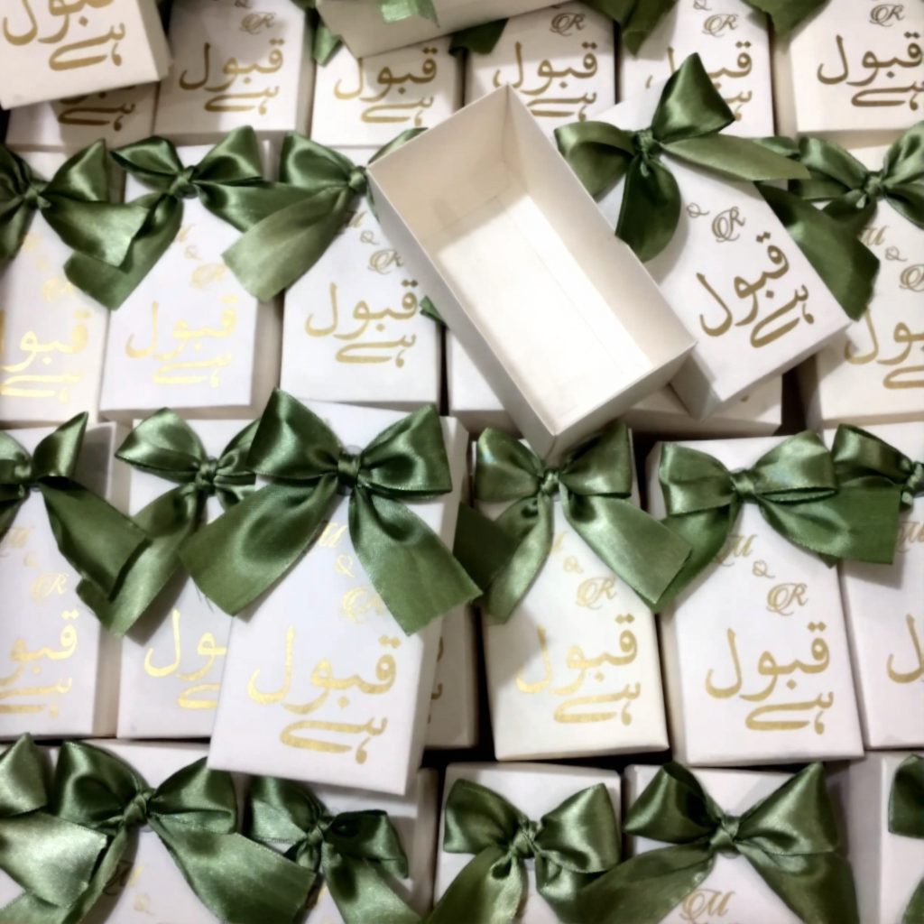 Ivory Qabool Hai Nikkah favor boxes with gold Urdu calligraphy and sage green satin bows for Pakistani and Muslim weddings.