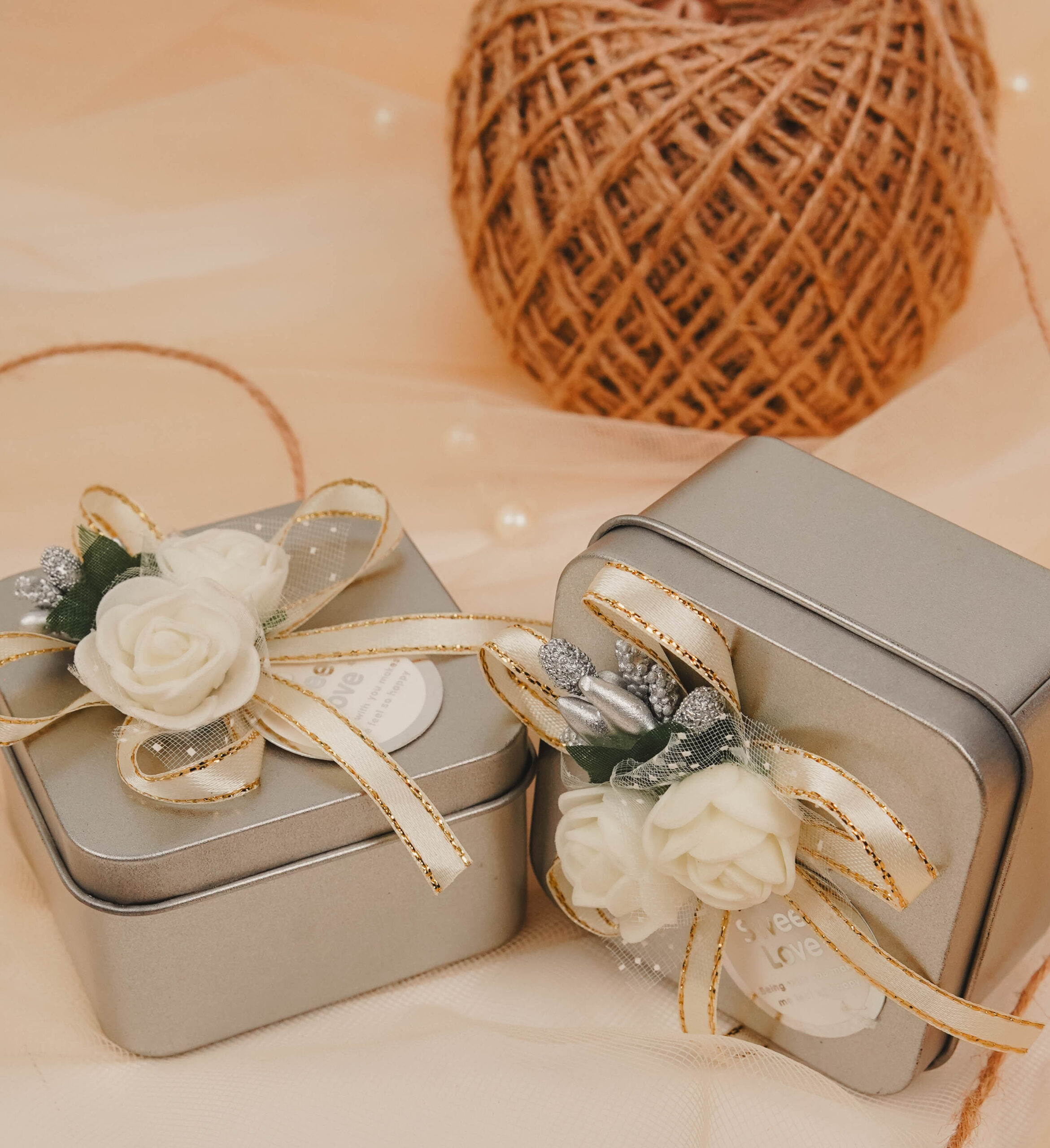 Silver floral tin favor boxes decorated with ivory flowers and gold-trimmed ribbons for Nikkah, Pakistani weddings and engagement celebrations.