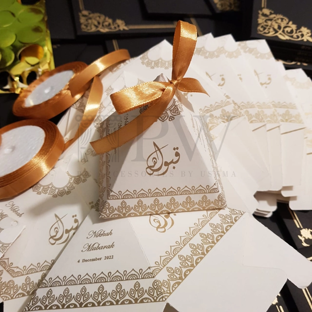 Ivory pyramid Nikkah favor boxes with gold decorative detailing and satin bows for personalized Pakistani and Muslim wedding favors.