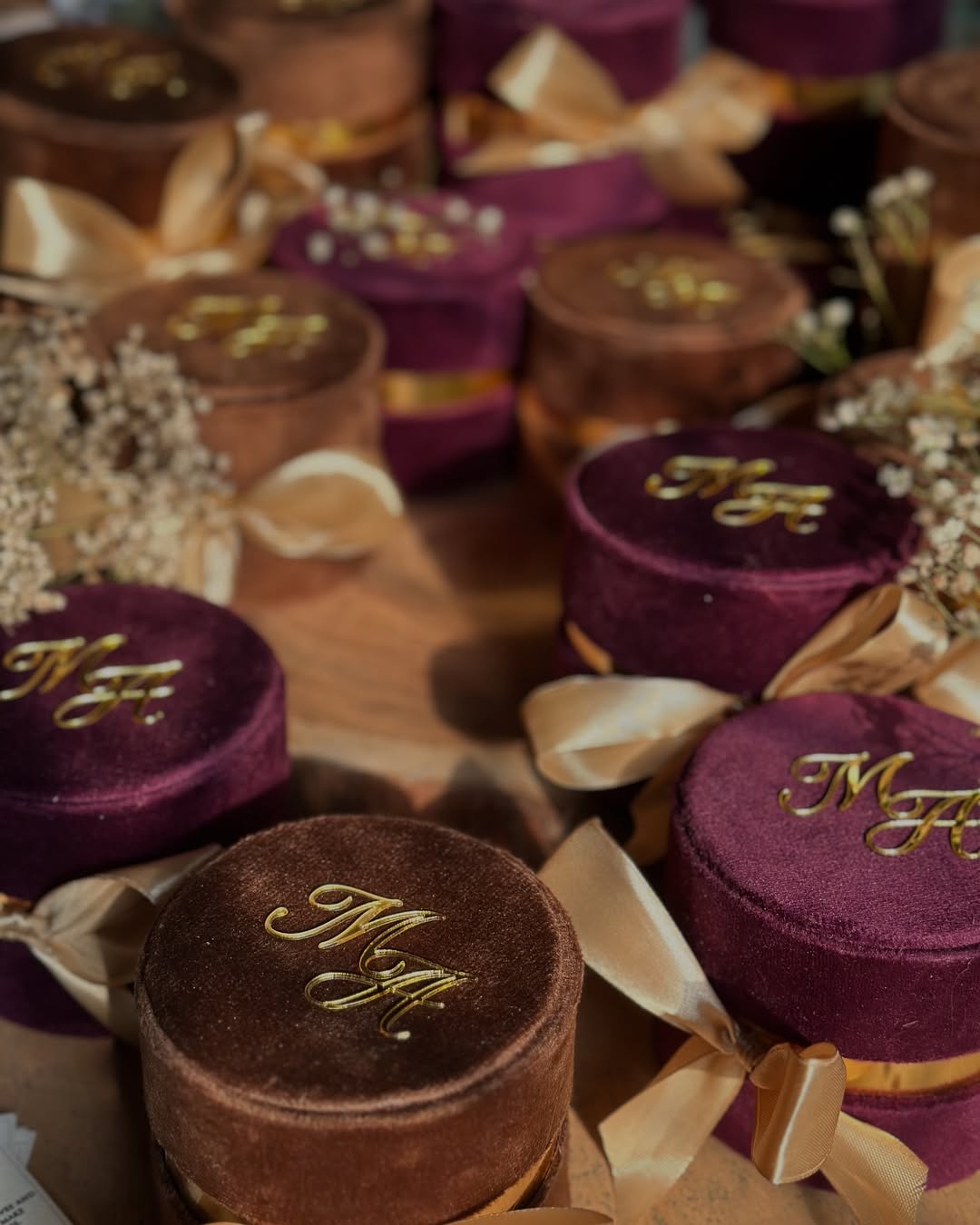 Burgundy and mocha round velvet Nikkah favor boxes personalized with gold initials and satin bows for Pakistani and Muslim weddings.
