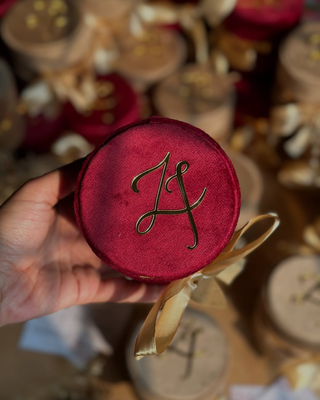 Burgundy and mocha round velvet Nikkah favor boxes personalized with gold initials and satin bows for Pakistani and Muslim weddings.