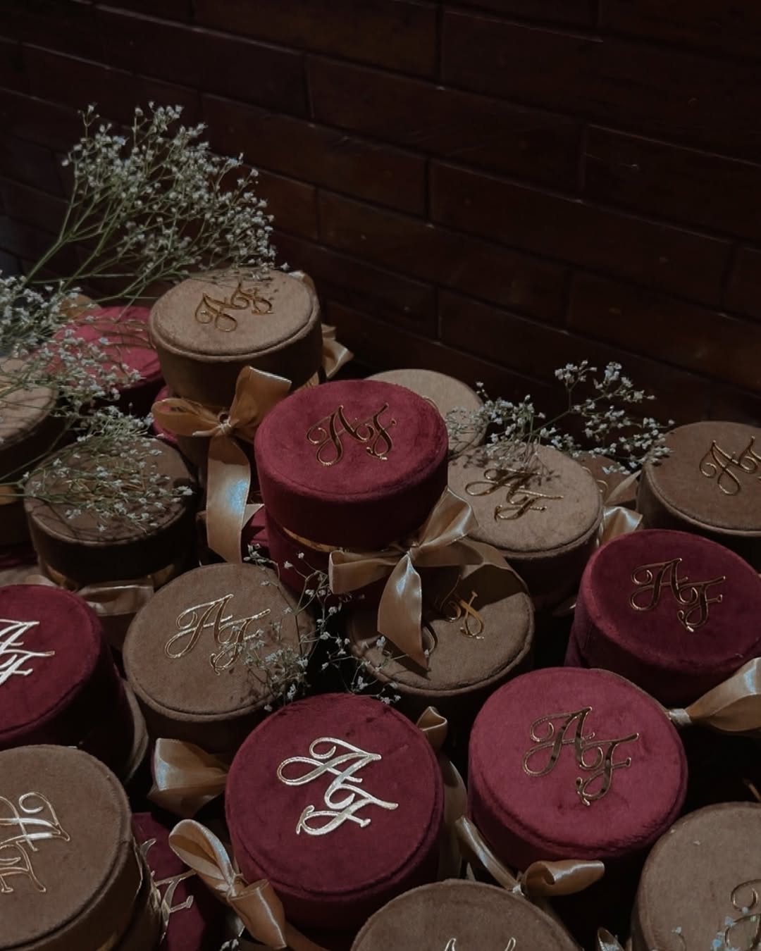 Burgundy and mocha round velvet Nikkah favor boxes personalized with gold initials and satin bows for Pakistani and Muslim weddings.
