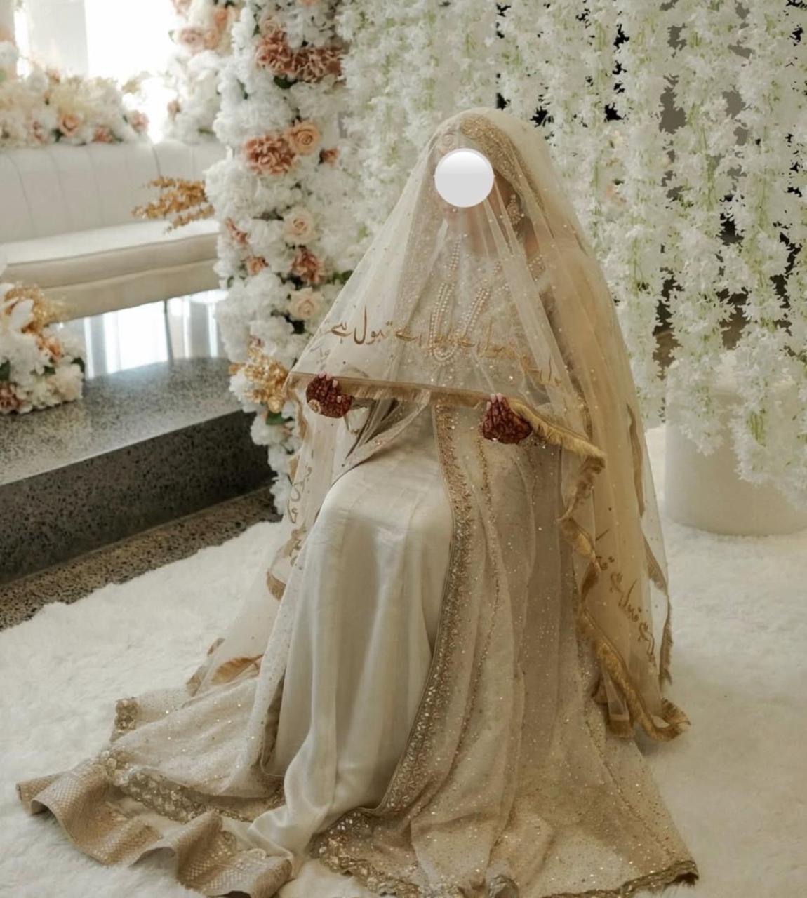 Ivory Pakistani bridal Nikkah dupatta featuring delicate sheer net fabric, gold embroidered borders, shimmering sequins, and Urdu calligraphy, elegantly draped over a Muslim bride during her wedding ceremony.