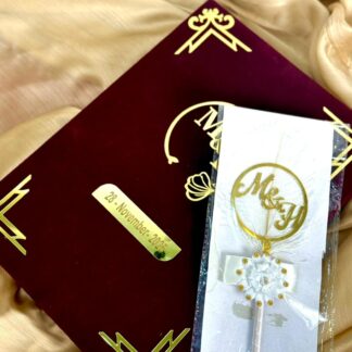 Personalized burgundy velvet Nikkah Nama folder with metallic gold couple's monogram, custom wedding date plaque, decorative gold corners, and matching white feather-style signing pen for Pakistani Muslim weddings.