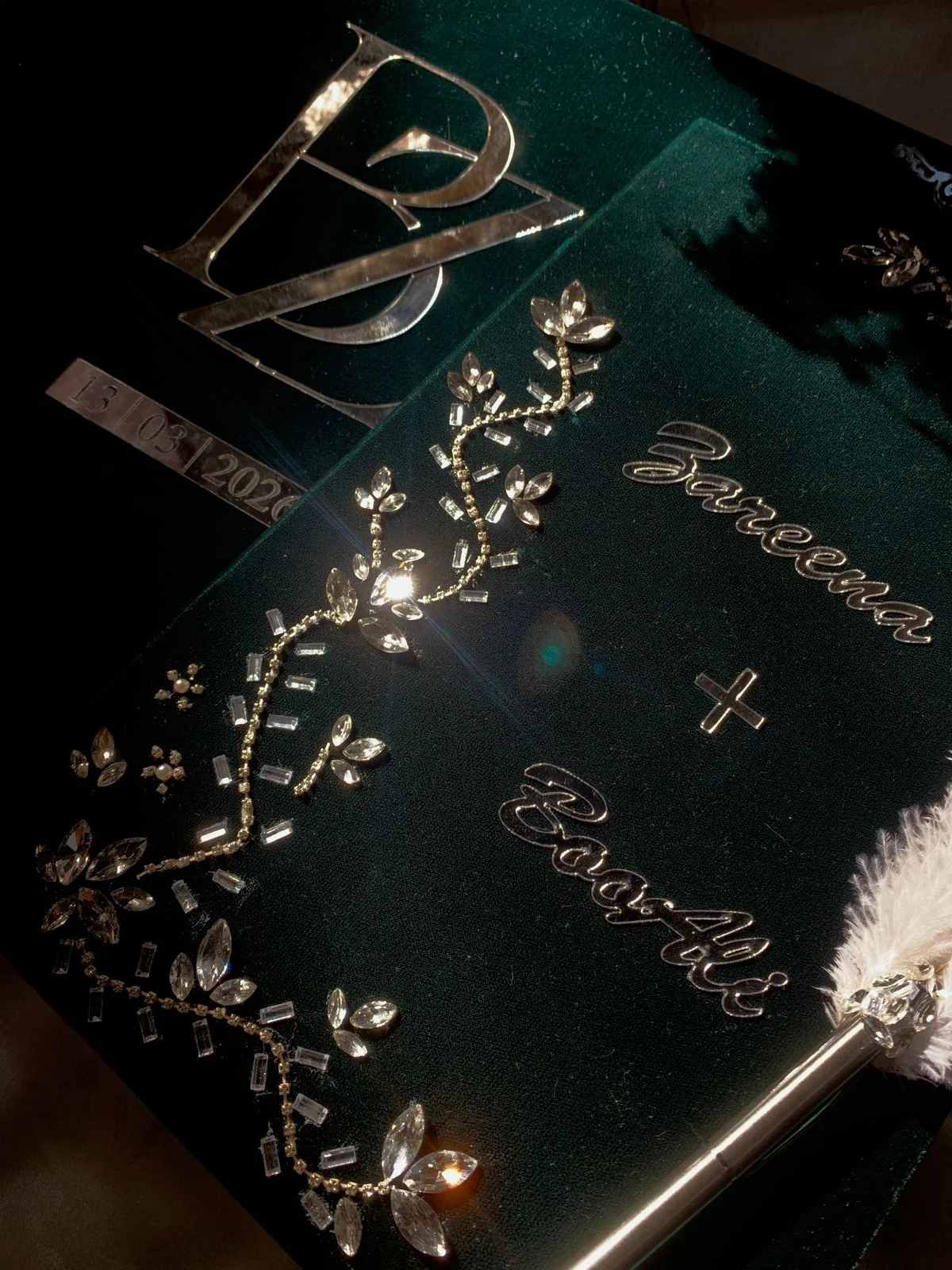Personalized emerald green velvet Nikkah Nama folder featuring silver couple's names, sparkling crystal floral vine embellishments, and a decorative silver-tone feather signing pen for Pakistani and Muslim wedding ceremonies.