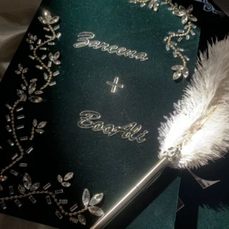 Personalized emerald green velvet Nikkah Nama folder featuring silver couple's names, sparkling crystal floral vine embellishments, and a decorative silver-tone feather signing pen for Pakistani and Muslim wedding ceremonies.