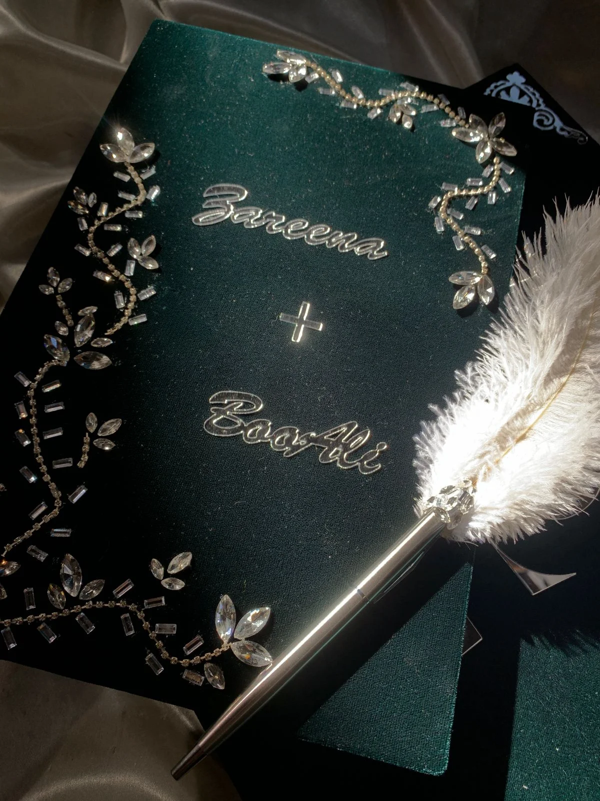 Personalized emerald green velvet Nikkah Nama folder featuring silver couple's names, sparkling crystal floral vine embellishments, and a decorative silver-tone feather signing pen for Pakistani and Muslim wedding ceremonies.