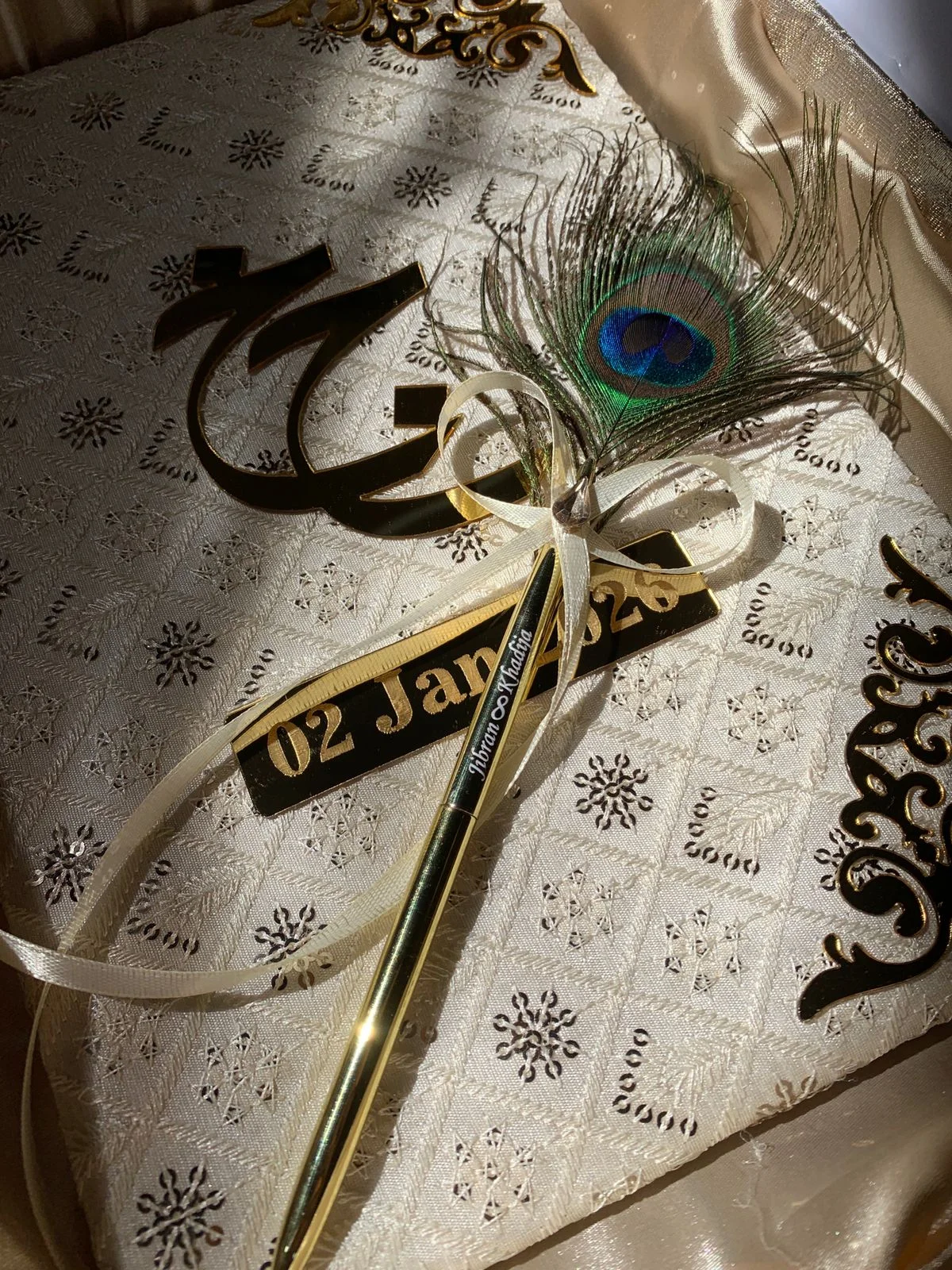 Luxury ivory embroidered Nikkah Nama folder with metallic gold calligraphy, ornate corner decorations, and a decorative signing pen, presented in a champagne-gold satin-lined gift box for Pakistani and Muslim wedding ceremonies.
