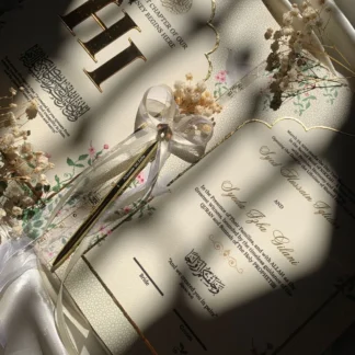 ersonalized ivory floral Nikkah Nama folder featuring a metallic gold monogram, elegant Quranic calligraphy, delicate pink floral illustrations, and a decorative gold-tone signing pen with ivory ribbons for Pakistani and Muslim wedding ceremonies.
