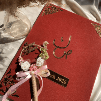 Personalized maroon velvet Nikkah Nama folder featuring metallic gold Urdu calligraphy, intricate ornamental gold corners, custom wedding date plaque, and decorative floral signing pen with pink satin ribbons for Pakistani and Muslim weddings in the USA.
