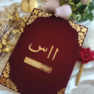 Personalized maroon velvet Nikkah Nama folder featuring metallic gold Urdu initials, a custom wedding date plaque, and ornate gold floral corner embellishments for Pakistani and Muslim wedding ceremonies.