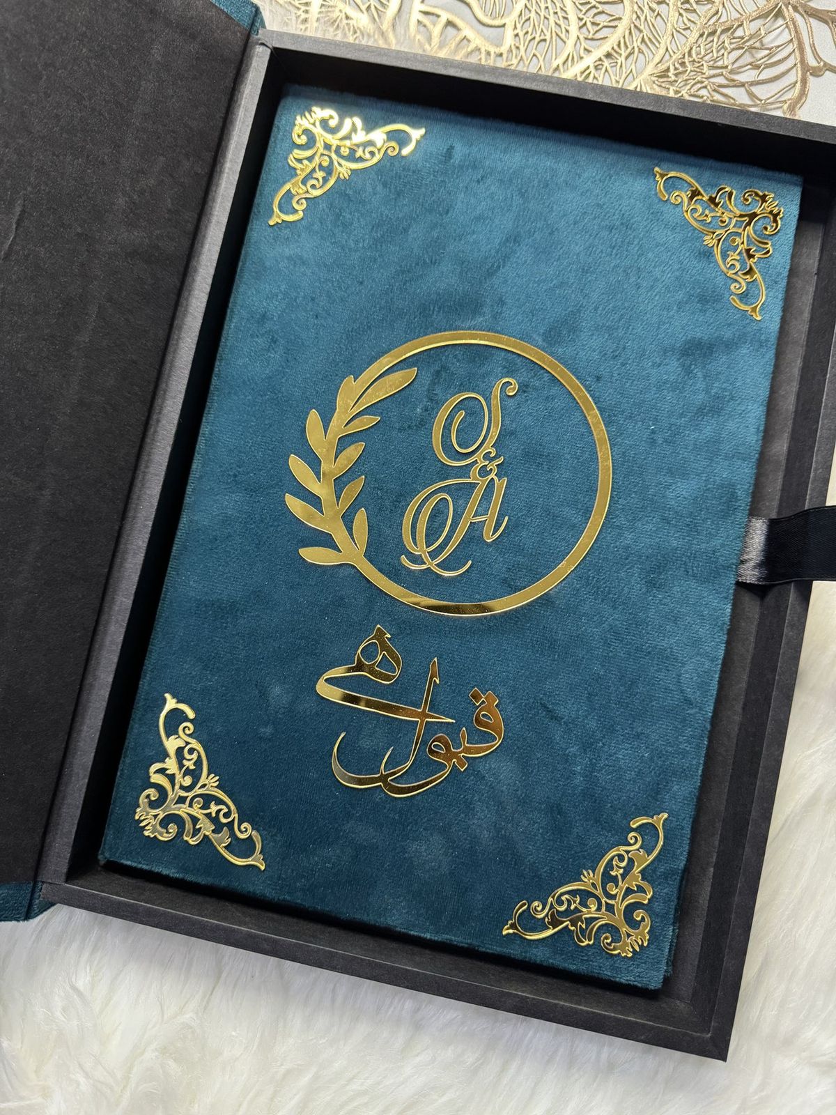 Personalized Nikkah Nama marriage certificate with intricate gold Islamic borders, Arabic calligraphy, and traditional bride-and-groom illustration inside a luxury teal blue folder.