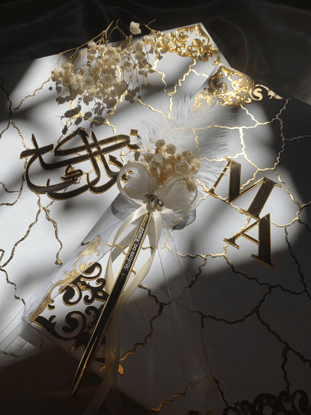Personalized white and gold marble Nikkah Nama folder featuring reflective gold couple initials, intricate ornamental gold corners, elegant marble-inspired veining, decorative floral signing pen, and champagne satin-lined presentation box for Pakistani and Muslim weddings in the USA.